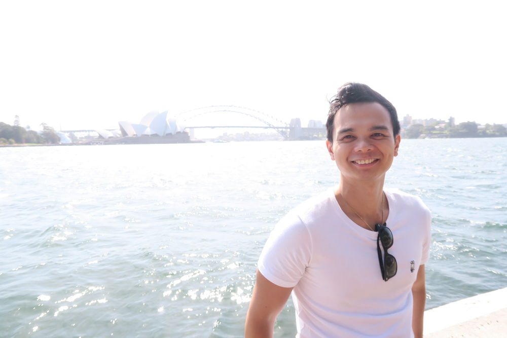 Matthew Alberto smiling on the Sydney harbour foreshore, with the Opera House and Harbour Bridge behind him